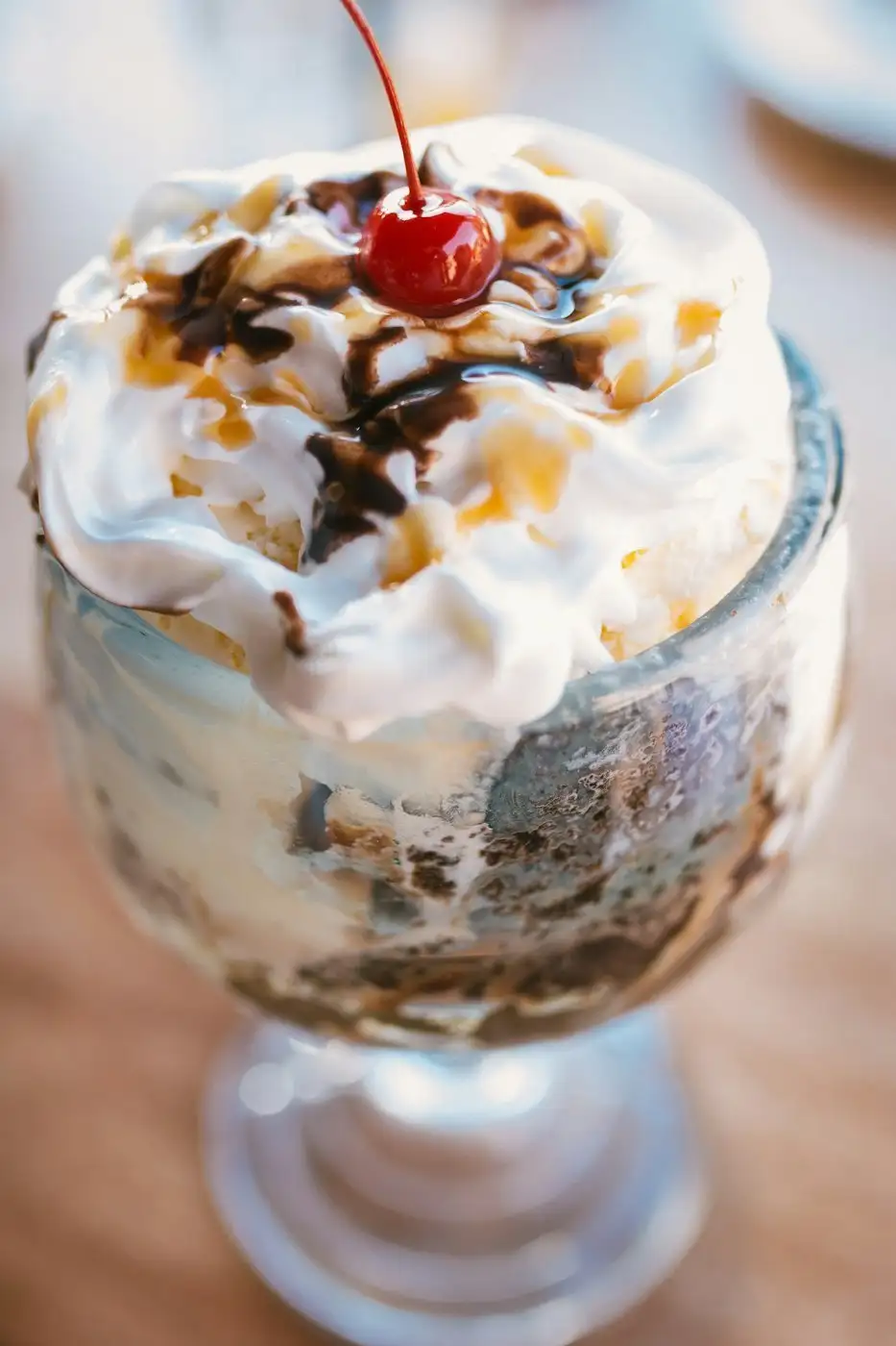 A sundae with whipped cream, chocolate and caramel sauce and a stemmed cherry