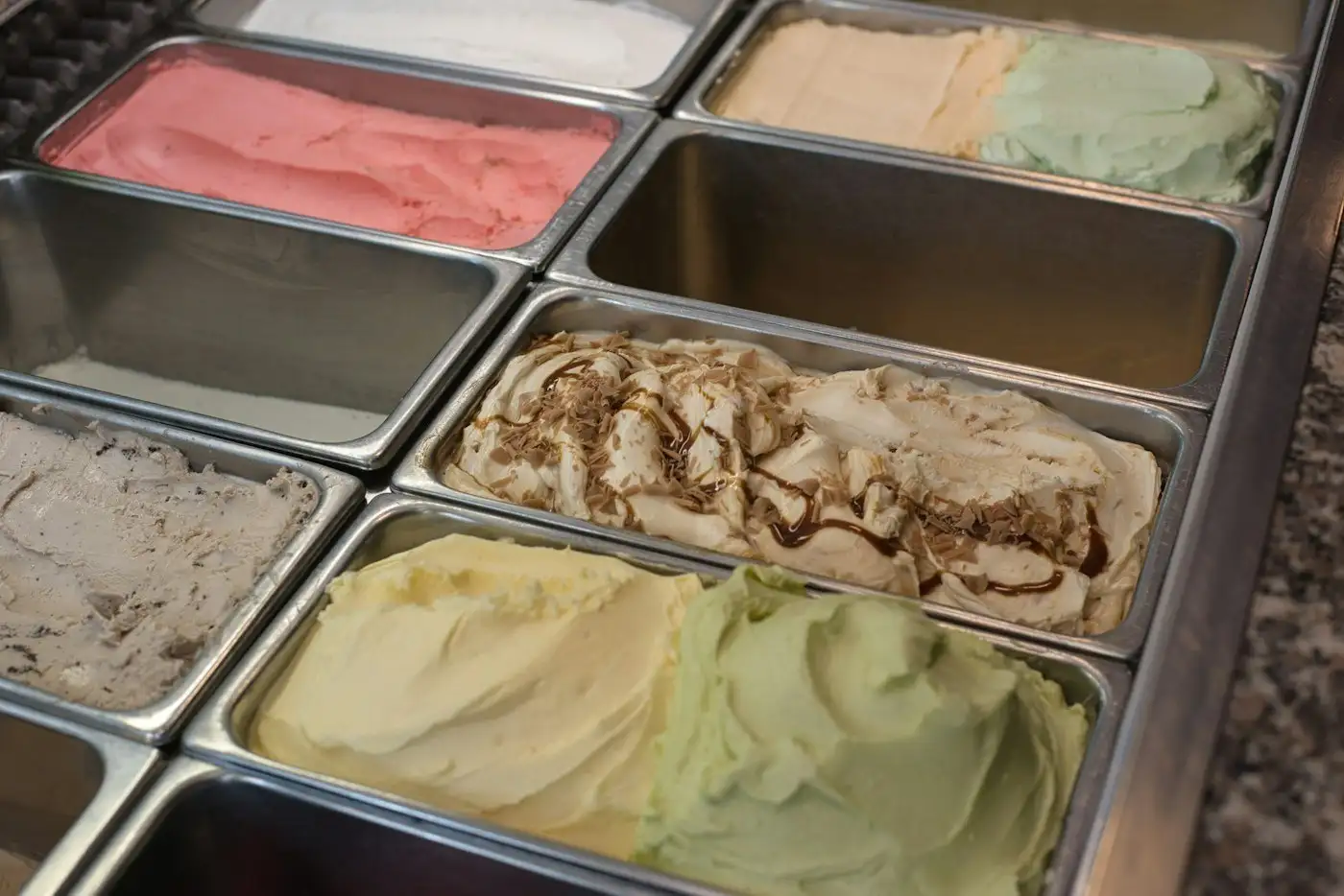 Steel pans of strawberry, vanilla, pistachio and caramel swirl ice cream in a dipping case