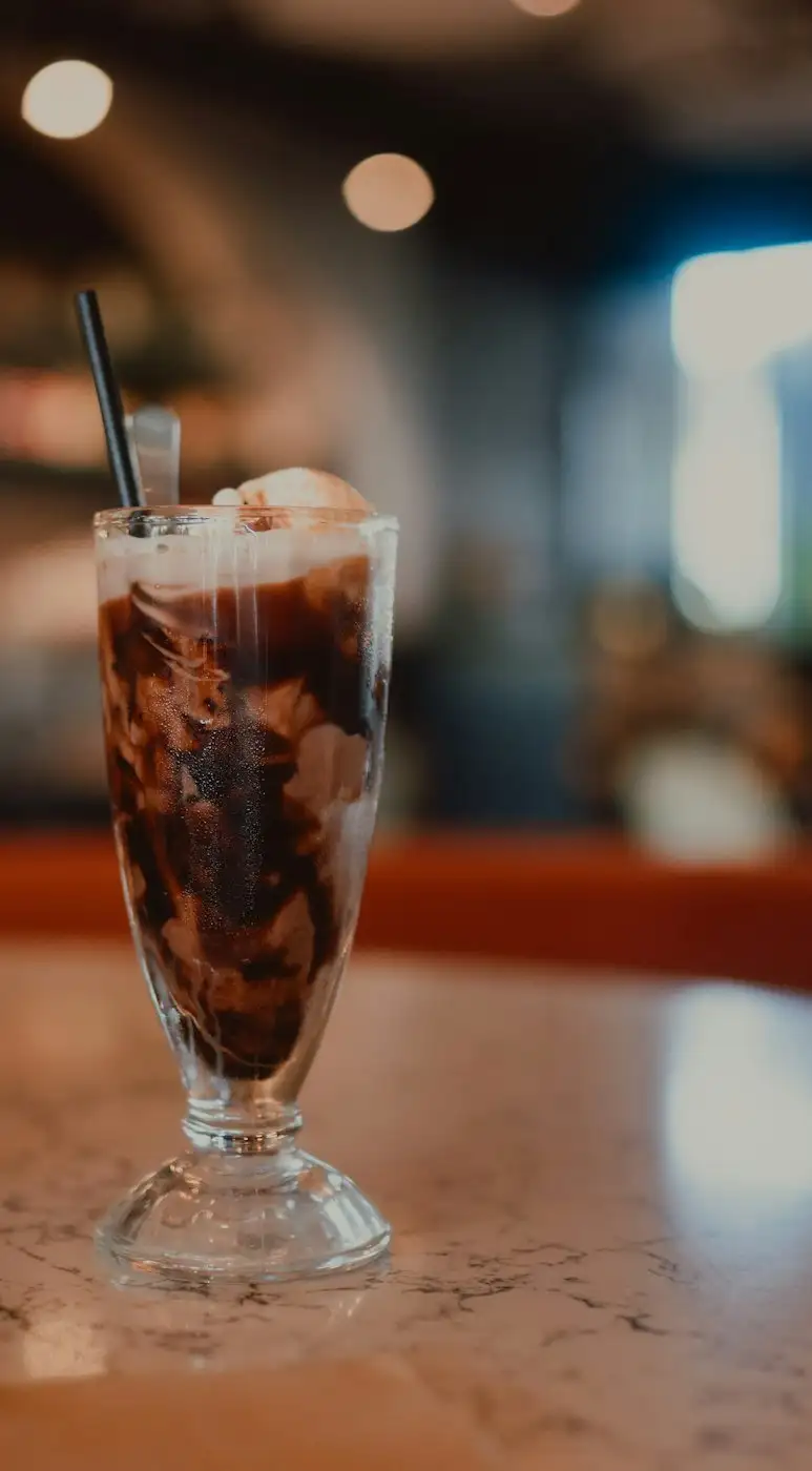 A chocolate ice cream soda in a tall fountain glass with a straw, on a marble counter
