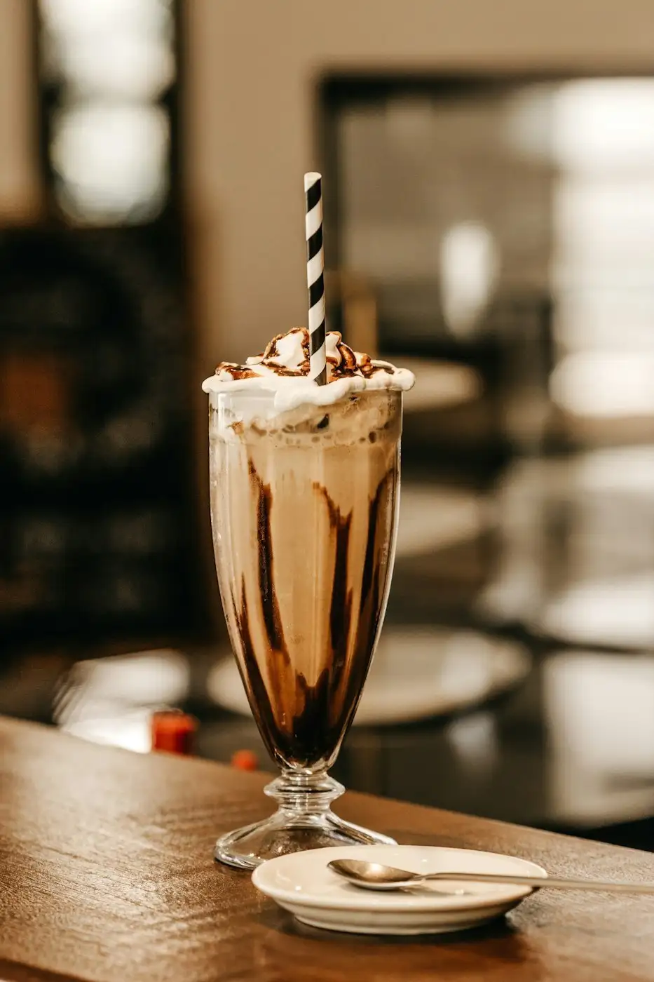 A chocolate milkshake with whipped cream and a striped straw in a tall footed glass
