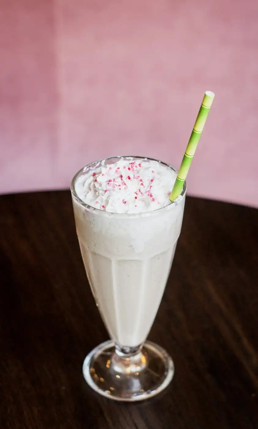 A vanilla milkshake with whipped cream, pink sprinkles and a green striped straw
